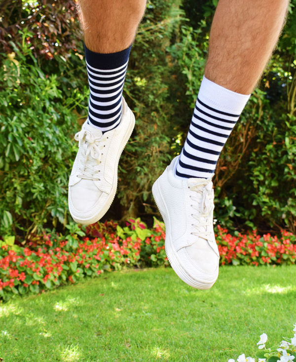Porté des chaussettes Made in France avec baskets blanches. Le mannequin saute les deux pieds sont bien visibles, l'un est marine rayé blanc, l'autre blanc rayé marine.