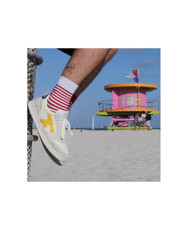 chaussettes Made in France portées sur une plage avec une paire de sneakers. La chaussette blanche est plus visible que la rouge.