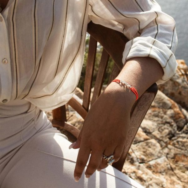 bracelet femme maille RECIF porté avec une chemise rayée et un pantalon blanc par une femme assise sur une chaise en bois
