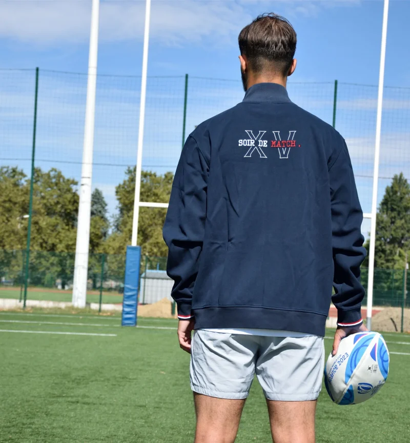 Photo de la veste sippée DIMITRI de dos portée sur un short sur un terrain de rugby face aux poteaux