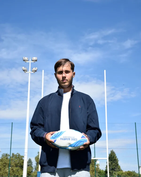 Photo portée de face de la veste zippée DIMITRI devant des poteaux de rugby. La veste est ouverte, le mannequin porte un ballon de rugby