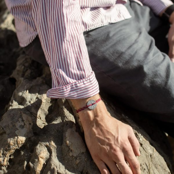 Photo cadrée serré du bracelet barrani porté par un homme portant une chemise rayée manche retroussée.